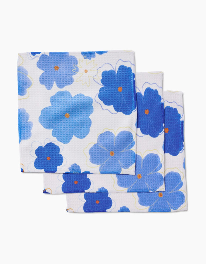 Three folded white Luxe Washcloths from Elana Gabrielle, Blue Blossoms design, feature large blue and light blue flowers with orange centers. Made with ultra-absorbent Geoweave technology for superior drying. Displayed on a white background.