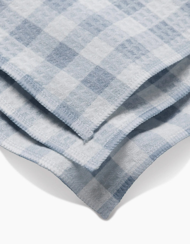 A close-up of the Aubrey Fairchild Blue Gingham washcloths, featuring soft light blue and white checks with visible edge stitching, highlights their ultra-absorbent Geoweave technology.