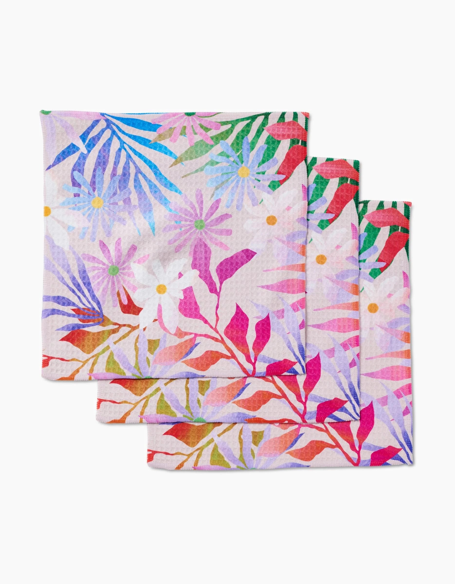 Three Bold Blossoms napkins by GEOMETRY are stacked, showcasing vibrant floral patterns in pink, purple, green, blue, red, and orange on a light background—crafted with ultra-absorbent Geoweave technology for top performance.