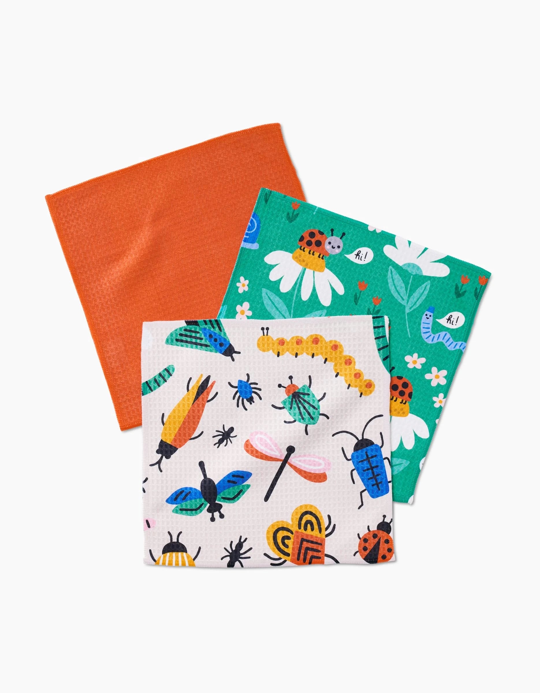 The Bugs washcloth set by Genna Blackburn includes three colorful dishcloths, each with ultra-absorbent Geoweave technology: one solid orange, one white with insects, and one green with ladybugs and flowers, arranged overlapping on a white background.