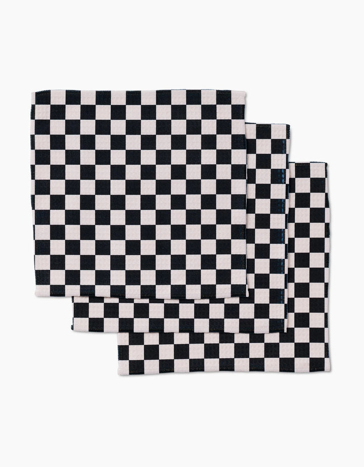 Four ultra-absorbent GEOMETRY Checkered cloth napkins, featuring a black and white checkerboard design, are neatly stacked with slight overlap on a white background.