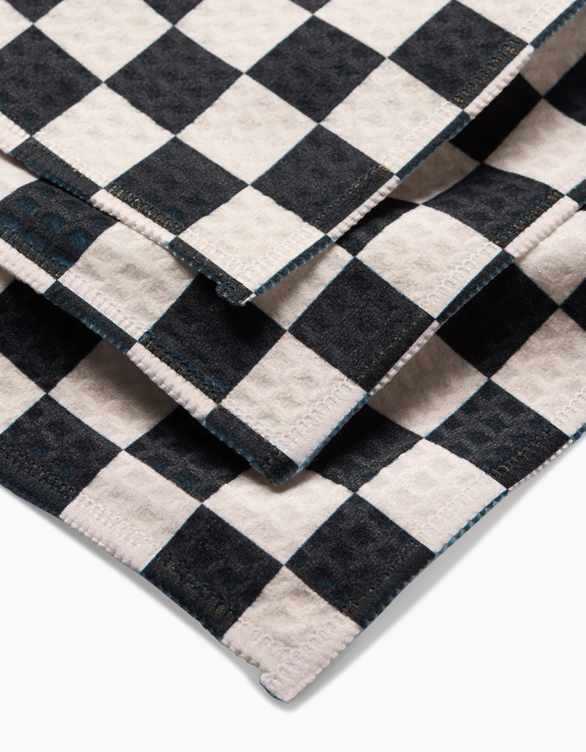 Close-up of three stacked GEOMETRY Checkered Luxe Washcloths, showcasing their textured fabric, ultra-absorbent Geoweave technology, and precise edge stitching in bold black and white patterns.