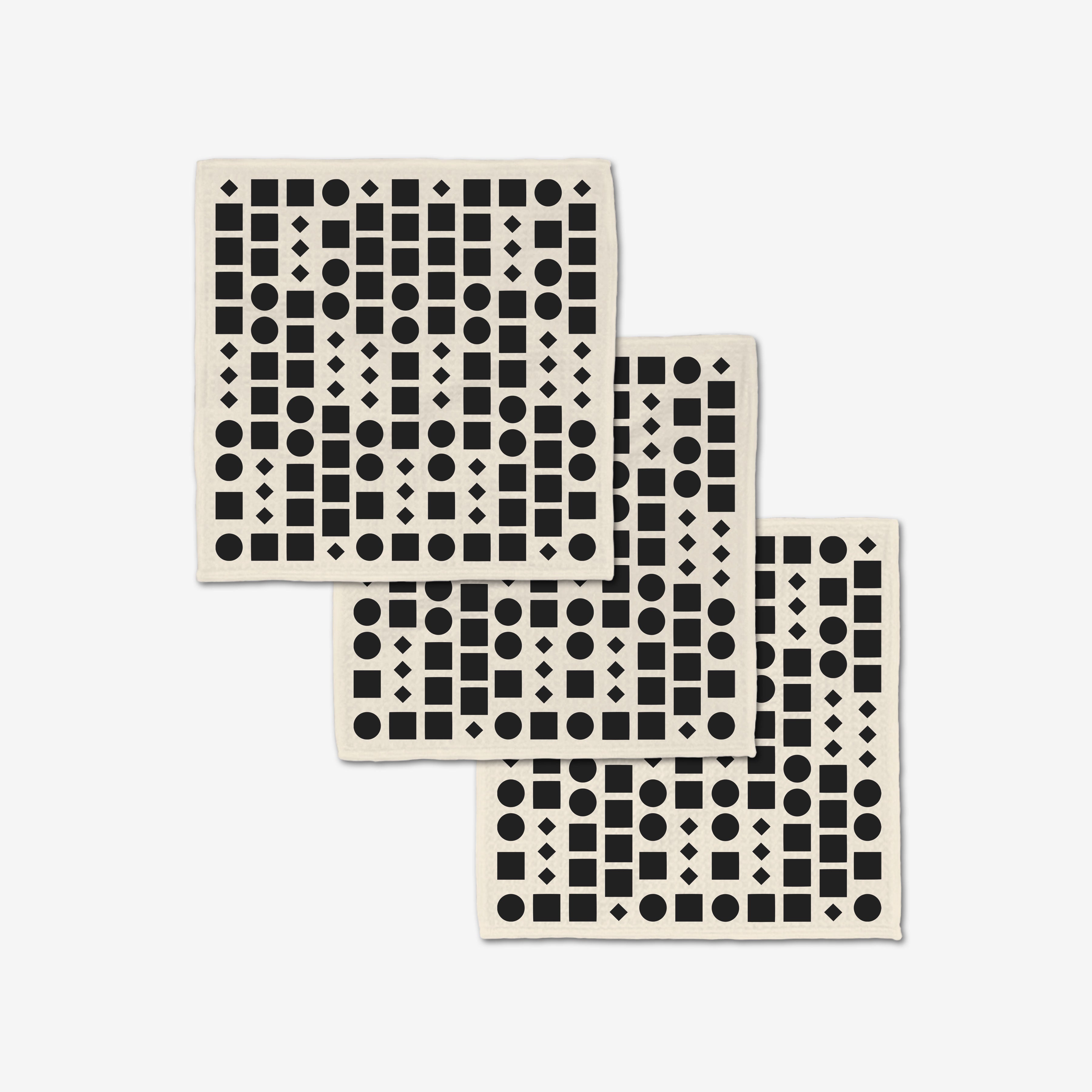 Three overlapping Coded washcloths by GEOMETRY showcase black circles, squares, triangles, and diamonds on white. Crafted from post-consumer recycled materials, these ultra-absorbent washcloths combine style and sustainability.