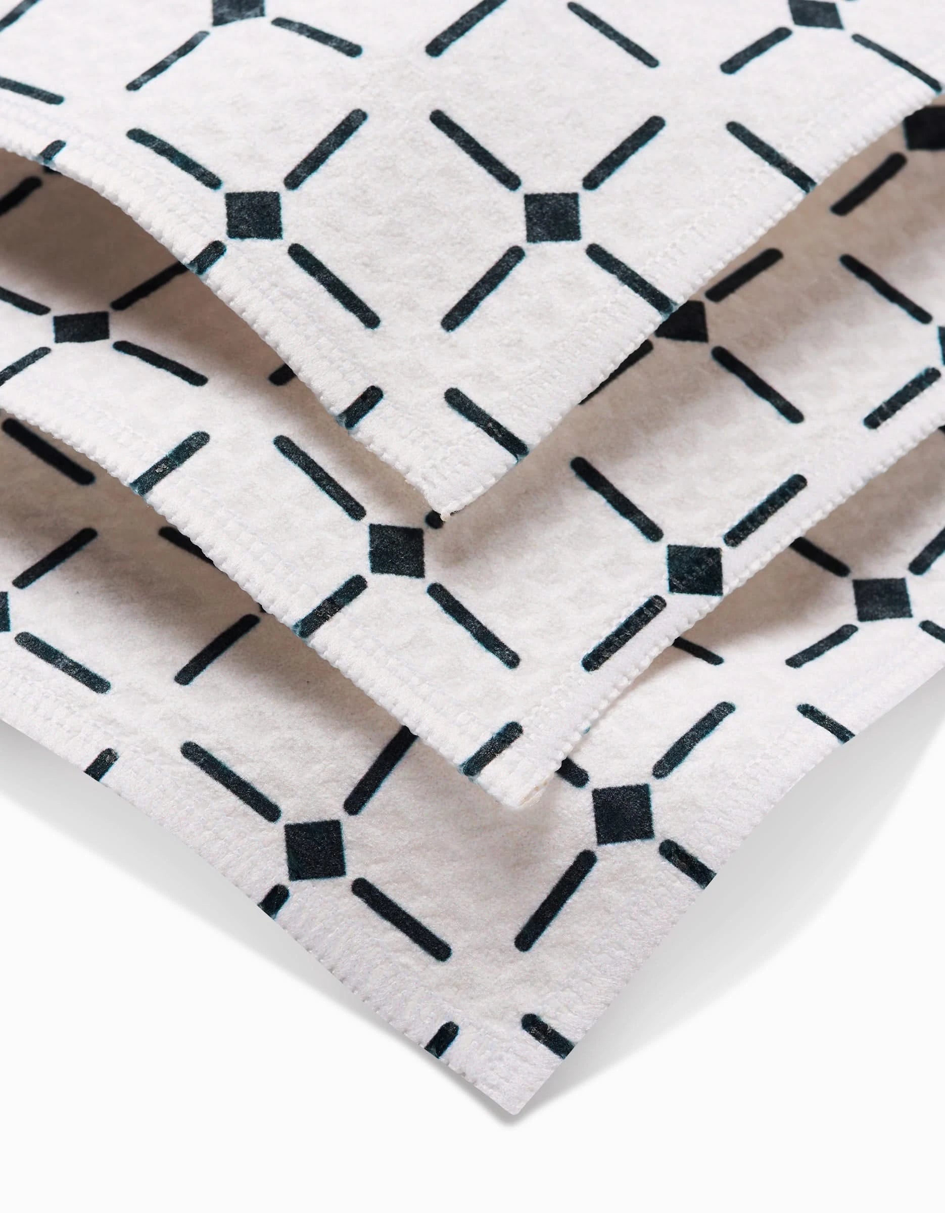Three stacked Collins Luxe Washcloths by Charlie Rowan Designs, featuring a repeating black diagonal line and diamond pattern, are shown up close to highlight their texture and ultra-absorbent Geoweave technology.