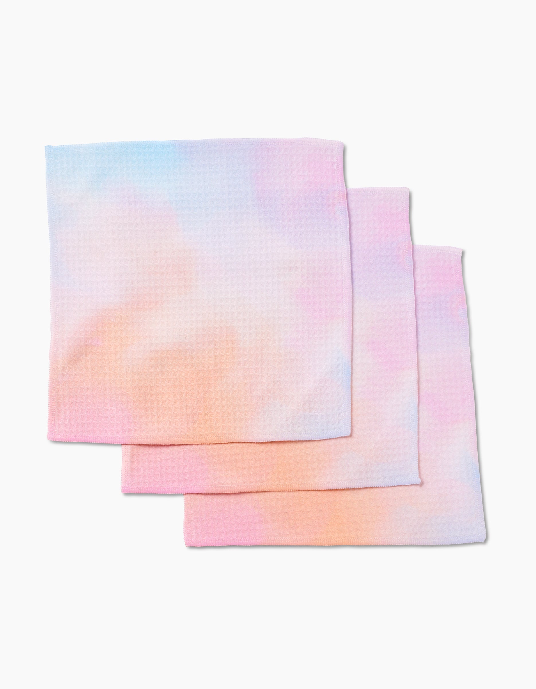 Three Cotton Candy Skies Luxe Washcloths by GEOMETRY, featuring a textured waffle pattern in soft pink, blue, orange, and purple pastels on white. Ultra-absorbent and stylish—perfect for blending form and function.