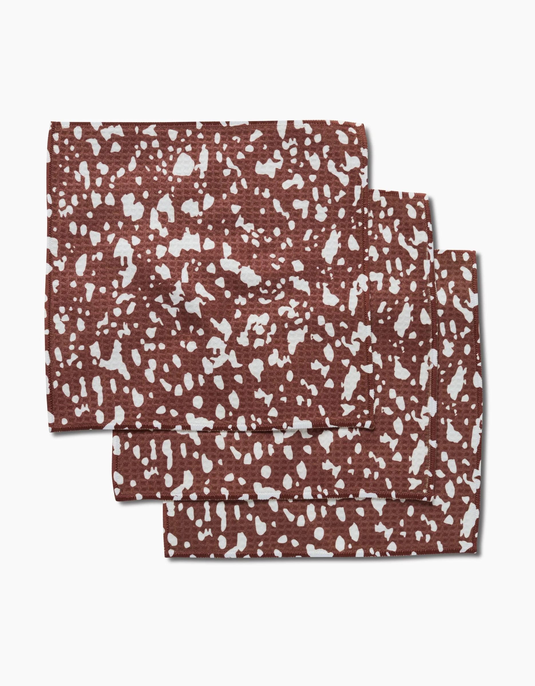Three folded Cowboy Horse Hide napkins by Hufton Studio, featuring an irregular white speckled pattern, are stacked on a white background. Made with Geoweave technology, these linens offer ultra-absorbent everyday elegance.