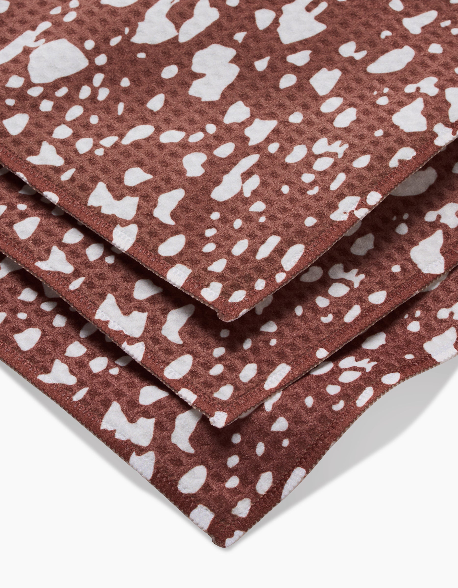 Three stacked Cowboy Horse Hide Luxe Washcloths by Hufton Studio, crafted with Geoweave technology, showcase brown fabric with irregular white spots like animal hide. Ultra-absorbent and stylish for any space, shown close up on a white background.