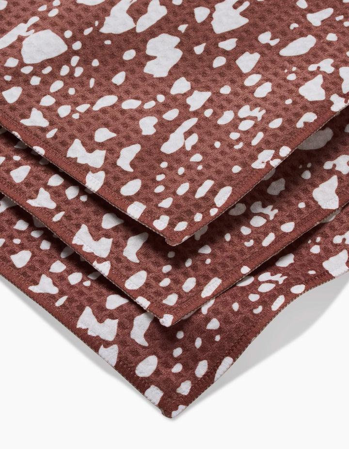 Three stacked Cowboy Horse Hide Luxe Washcloths by Hufton Studio, crafted with Geoweave technology, showcase brown fabric with irregular white spots like animal hide. Ultra-absorbent and stylish for any space, shown close up on a white background.