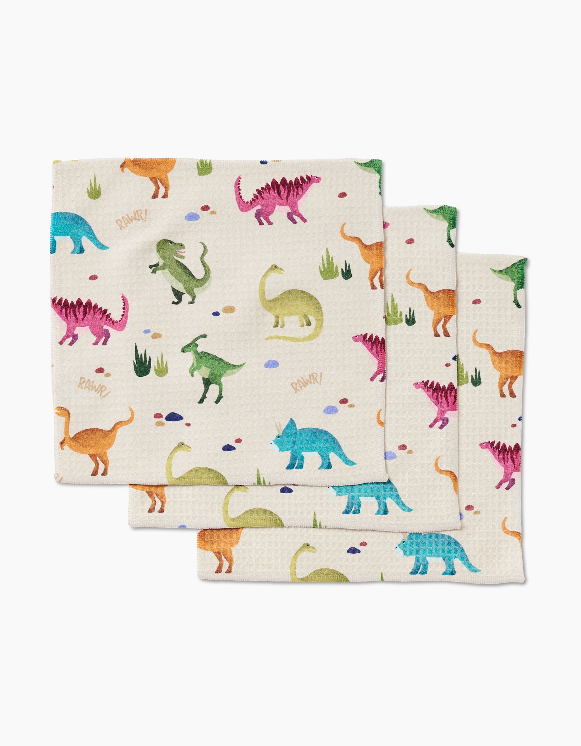 The GEOMETRY Dancing Dinos set includes three ultra-absorbent cloth napkins with a colorful dinosaur, grass, and rock pattern on white, made with Geoweave technology—perfect for adding fun to any mealtime.