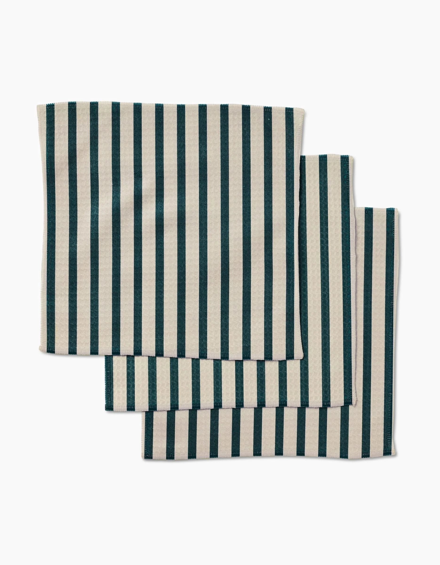 Three GEOMETRY Deep Green Stripes napkins, beige with vertical dark green stripes and made from post-consumer recycled materials, are stacked neatly and slightly overlapping on a white background.