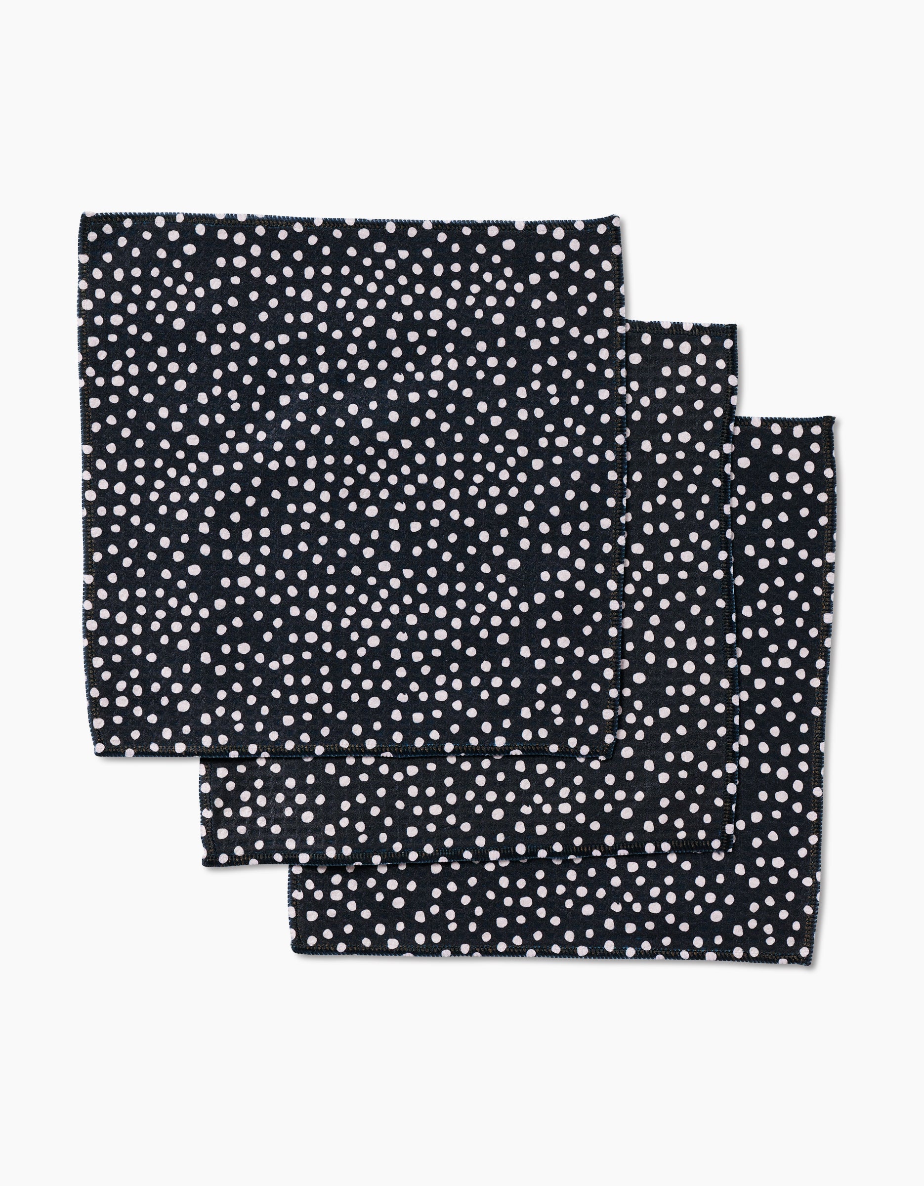 Three stacked GEOMETRY Dotty Black cloth napkins, featuring small white polka dots on black, crafted with Geoweave technology for exceptional absorbency.