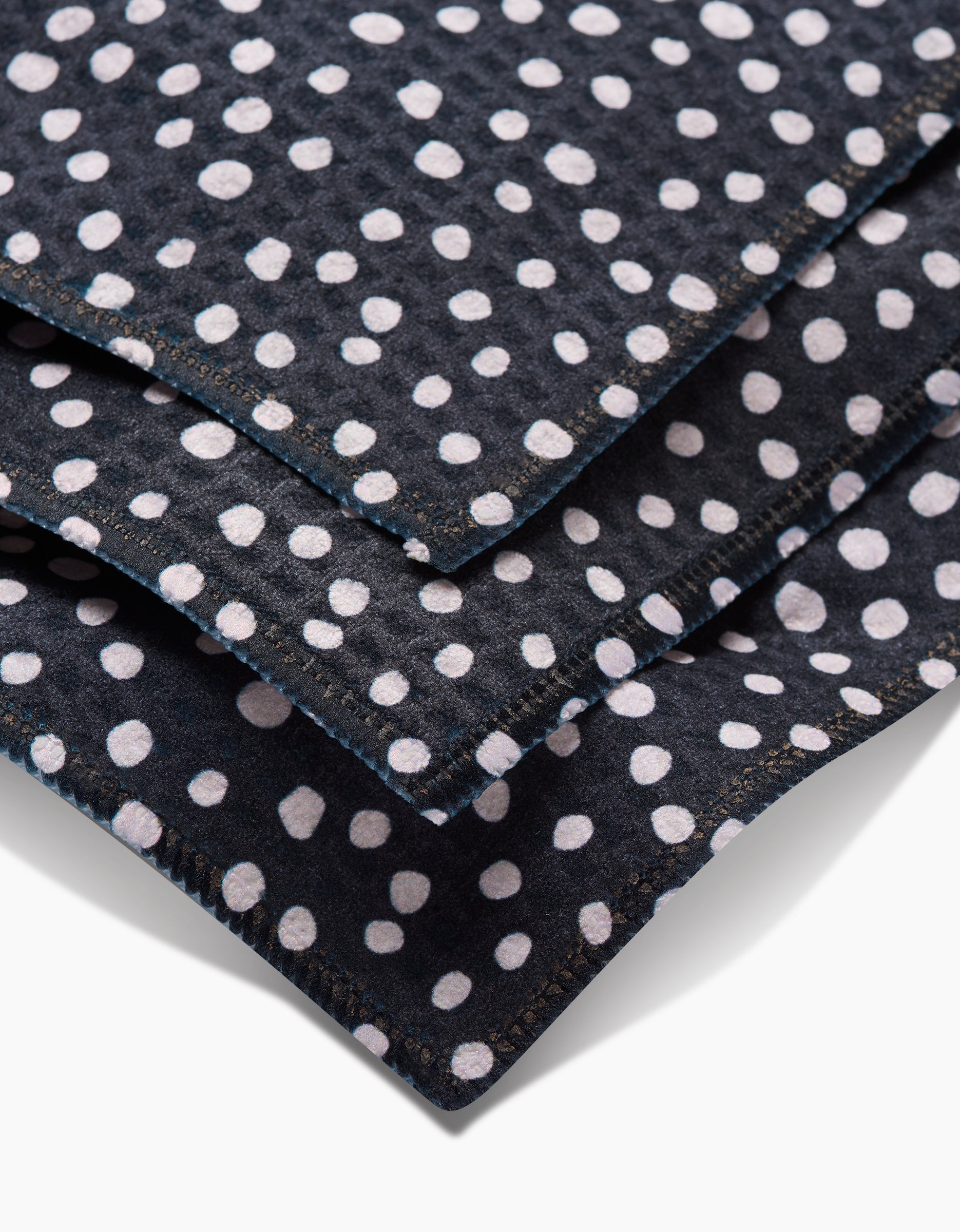 Three overlapping pieces of Dotty Black fabric by GEOMETRY, featuring white polka dots, shown close up to highlight texture and edge stitching—crafted with ultra-absorbent Geoweave technology for superior softness.