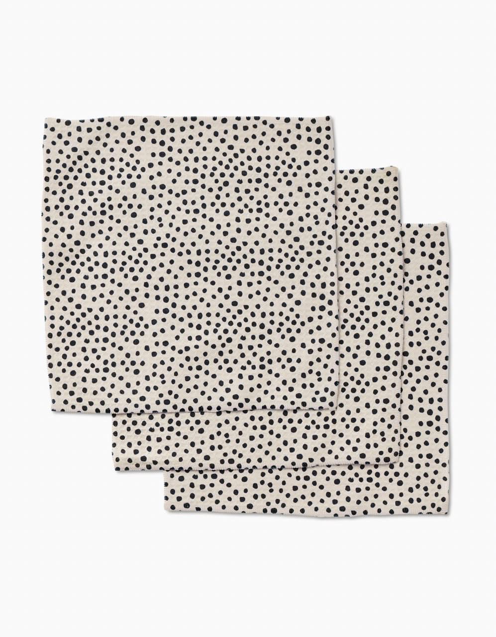 Three Dotty Tan napkins by GEOMETRY, made with ultra-absorbent Geoweave technology, feature a tan background with small, scattered black dots and are shown stacked slightly offset on white.