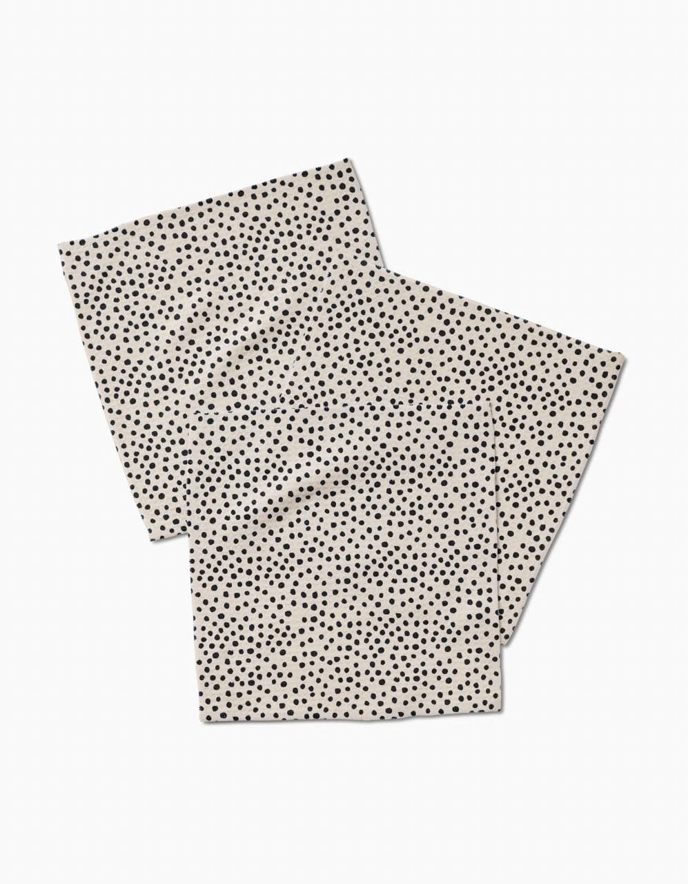 Two Dotty Tan rectangular napkins by GEOMETRY, in beige with small black polka dots, overlap on a white background. Made with ultra-absorbent Geoweave technology for top performance and stylish appeal.