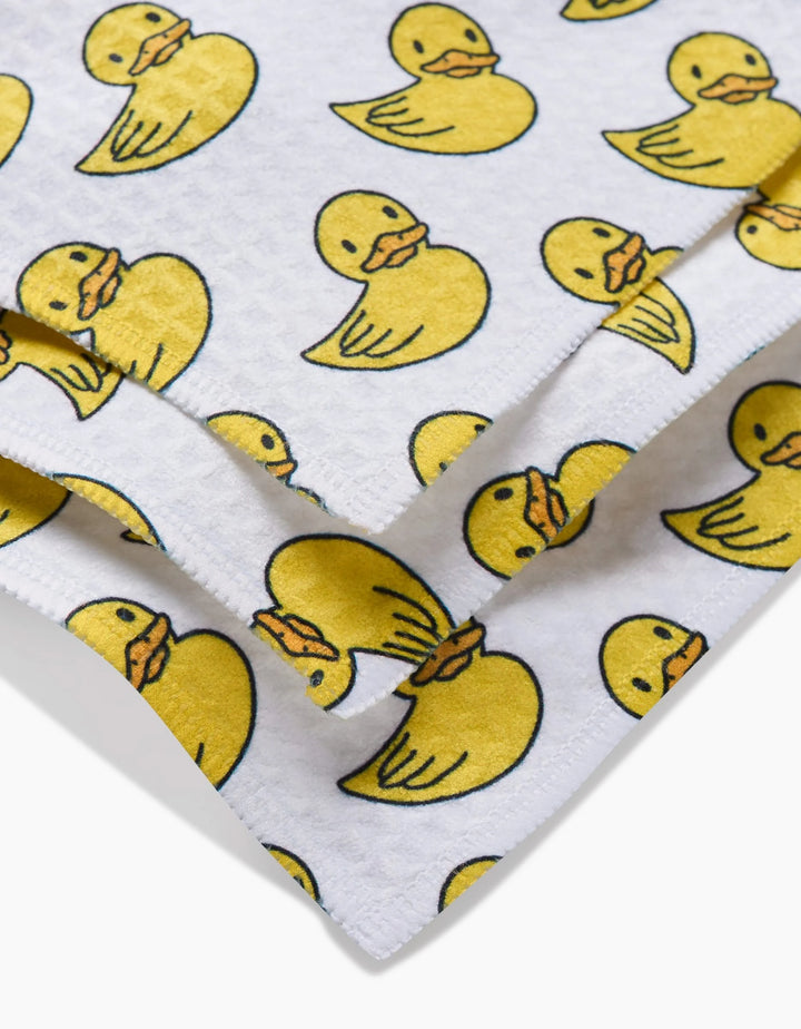 A close-up of GEOMETRYs Duckies washcloth, made from ultra-absorbent recycled materials and featuring a repeating yellow rubber duck pattern.