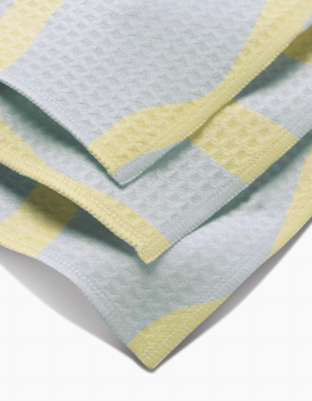 A close-up of GEOMETRYs Eclipse Twist washcloths, featuring an ultra-absorbent waffle texture with a light blue base and wavy yellow stripes.