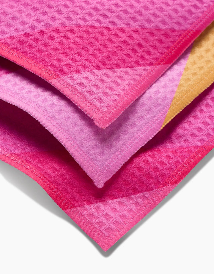 The GEOMETRY Electric Pink washcloth set features three stacked waffle-patterned fabrics in pink, purple, and orange shades, each with neatly finished edges for a stylish and ultra-soft touch.