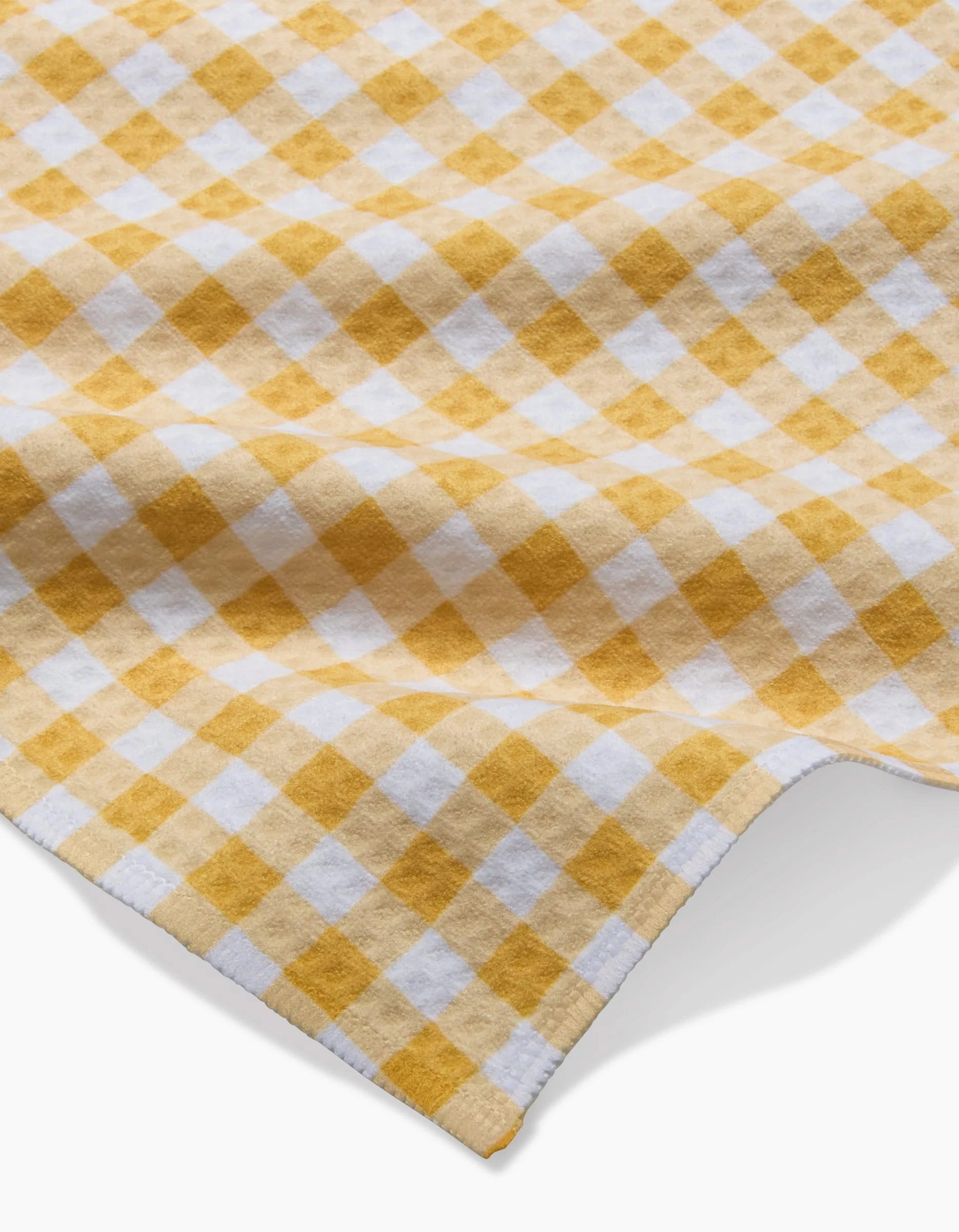 A close-up of the Golden Plaid Luxe Washcloth by Danelys Sidron, featuring a yellow and white plaid pattern with a soft, textured Geoweave fabric, slightly wrinkled to highlight its repeating checkered design.