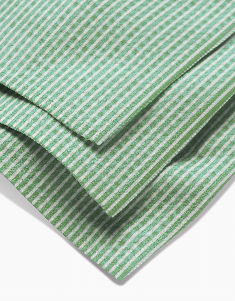 Close-up of folded GEOMETRY Half and Half Luxe Washcloth, featuring a green and white striped pattern with ultra-absorbent Geoweave technology. Three diagonal layers overlap on a white background.