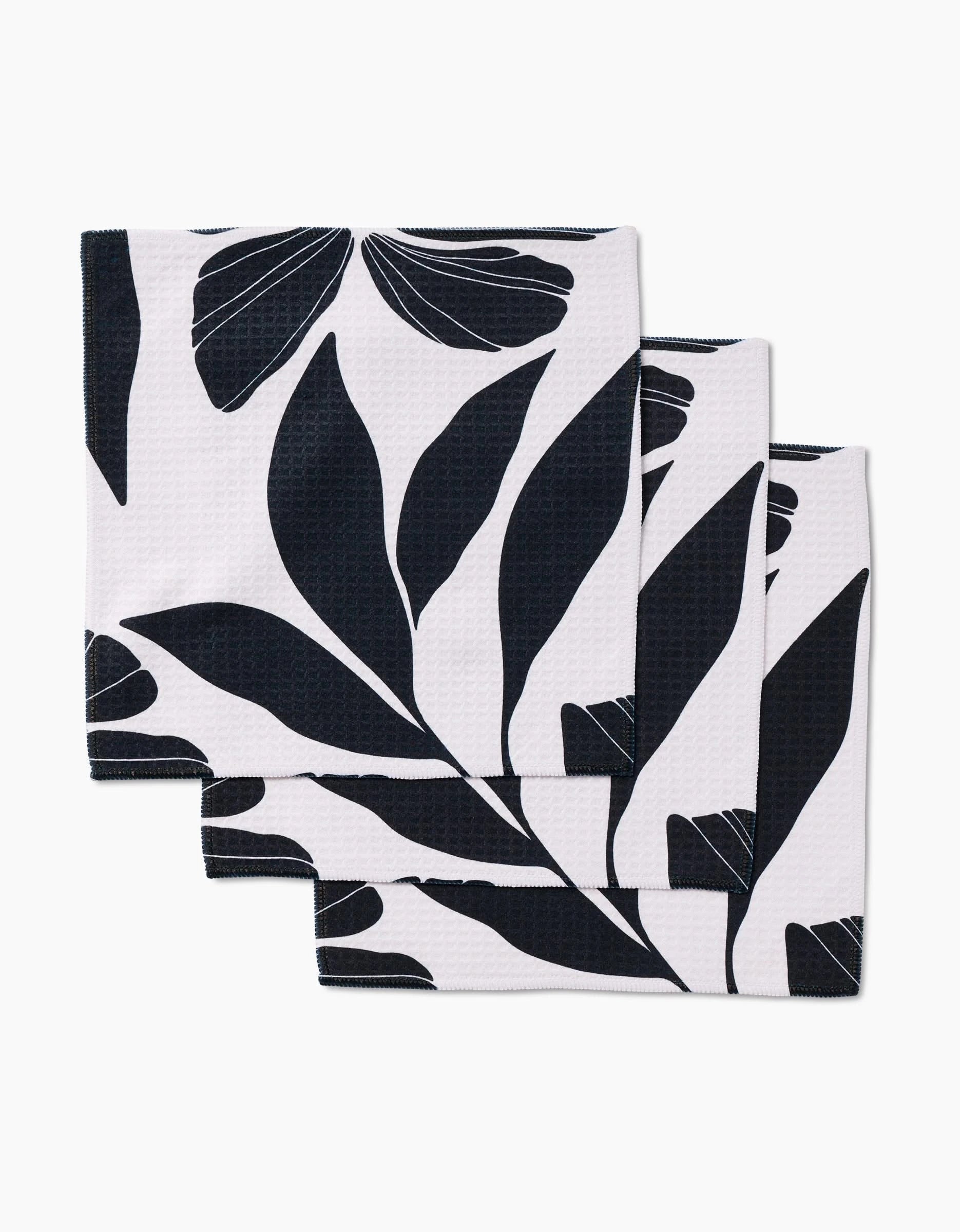 Three Harmony kitchen towels by GEOMETRY, made from recycled materials with a black botanical leaf pattern, are stacked slightly overlapping on a white background.