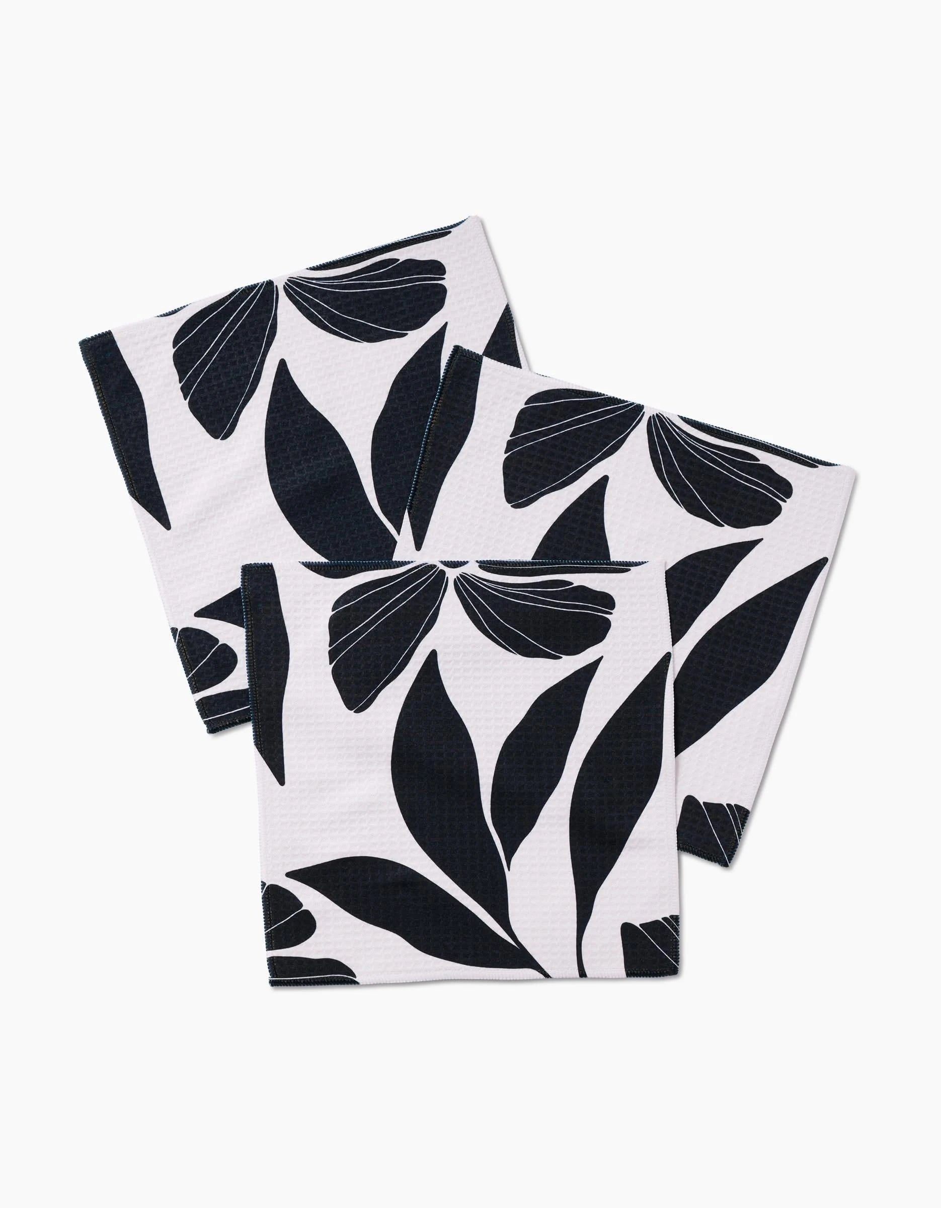 Three ultra-absorbent Harmony cloth napkins by GEOMETRY, featuring a bold black leaf pattern on white, are arranged overlapped on a white background.