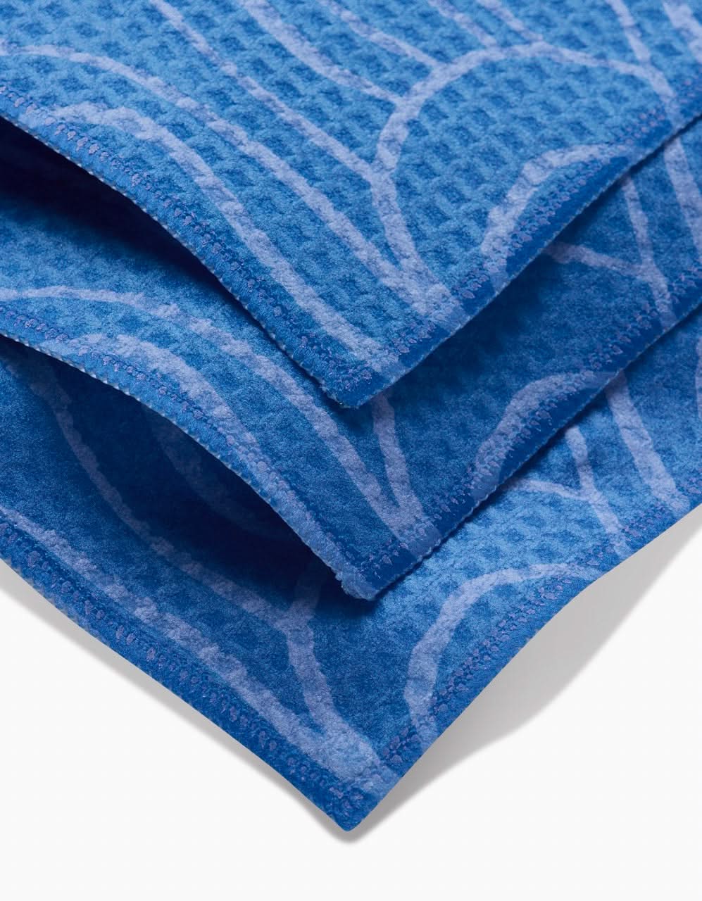 Close-up of Sareka Uniques High Tide ultra-absorbent blue towels with a textured waffle weave and lighter blue abstract-edged pattern, set against a white background—ideal for bringing Luxe Washcloth style to your bathroom.