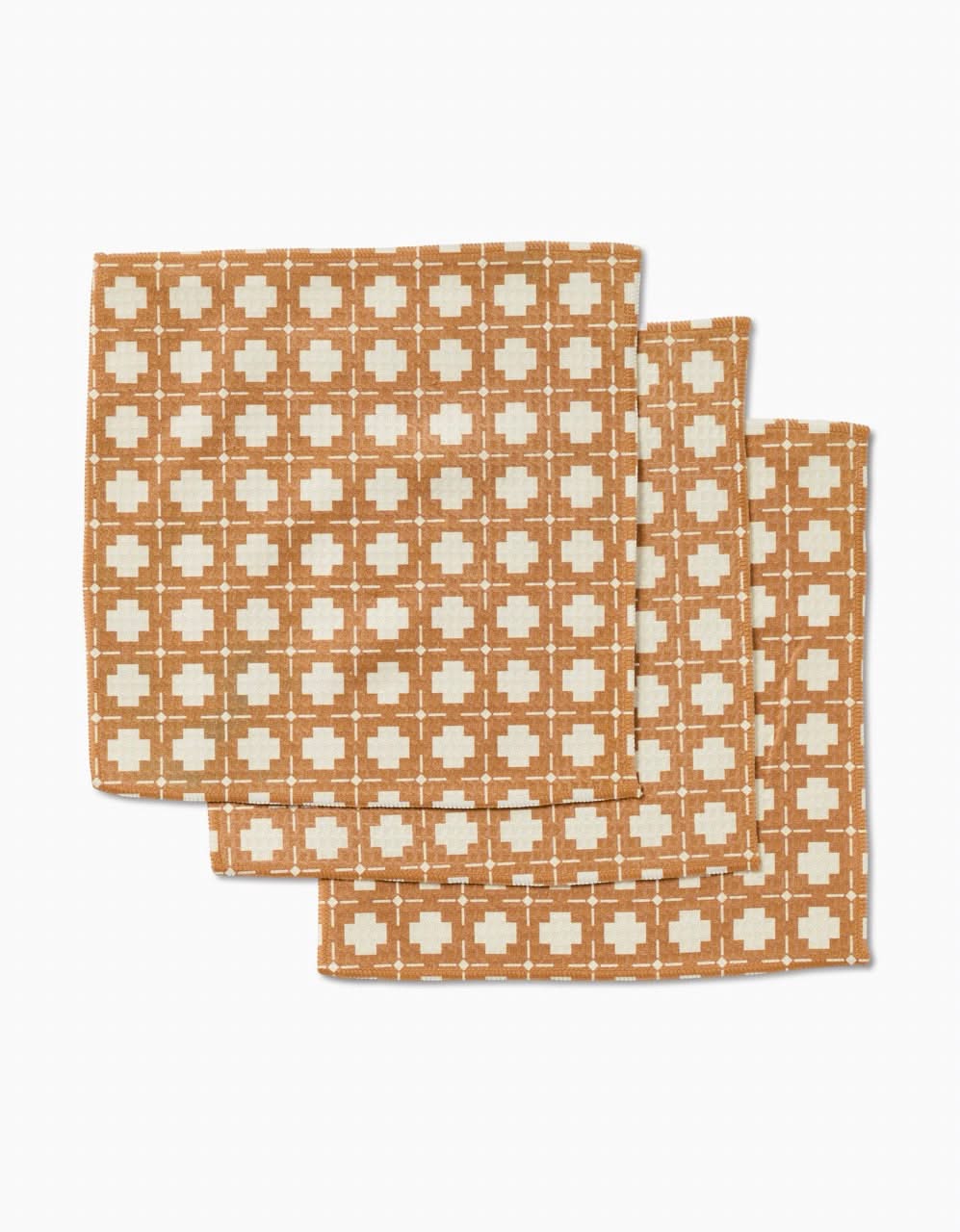 Three overlapping Jackson napkins by Charlie Rowan Designs, made from recycled materials, display a brown and cream geometric grid with cream crosses on a brown background, arranged on a white surface.