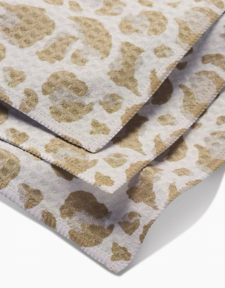 Close-up of overlapping GEOMETRY Light Leopard Luxe Washcloths with a beige and light brown animal print, crafted from ultra-absorbent Geoweave fabric for a soft, textured feel.