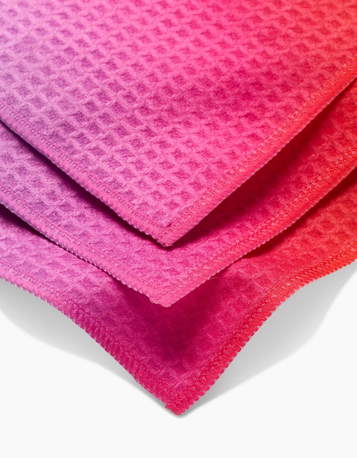 Three GEOMETRY Lively Hue washcloths in pink, purple, and red are stacked on white. With stitched edges and a waffle-like texture, these ultra-absorbent cloths feature advanced Geoweave technology.