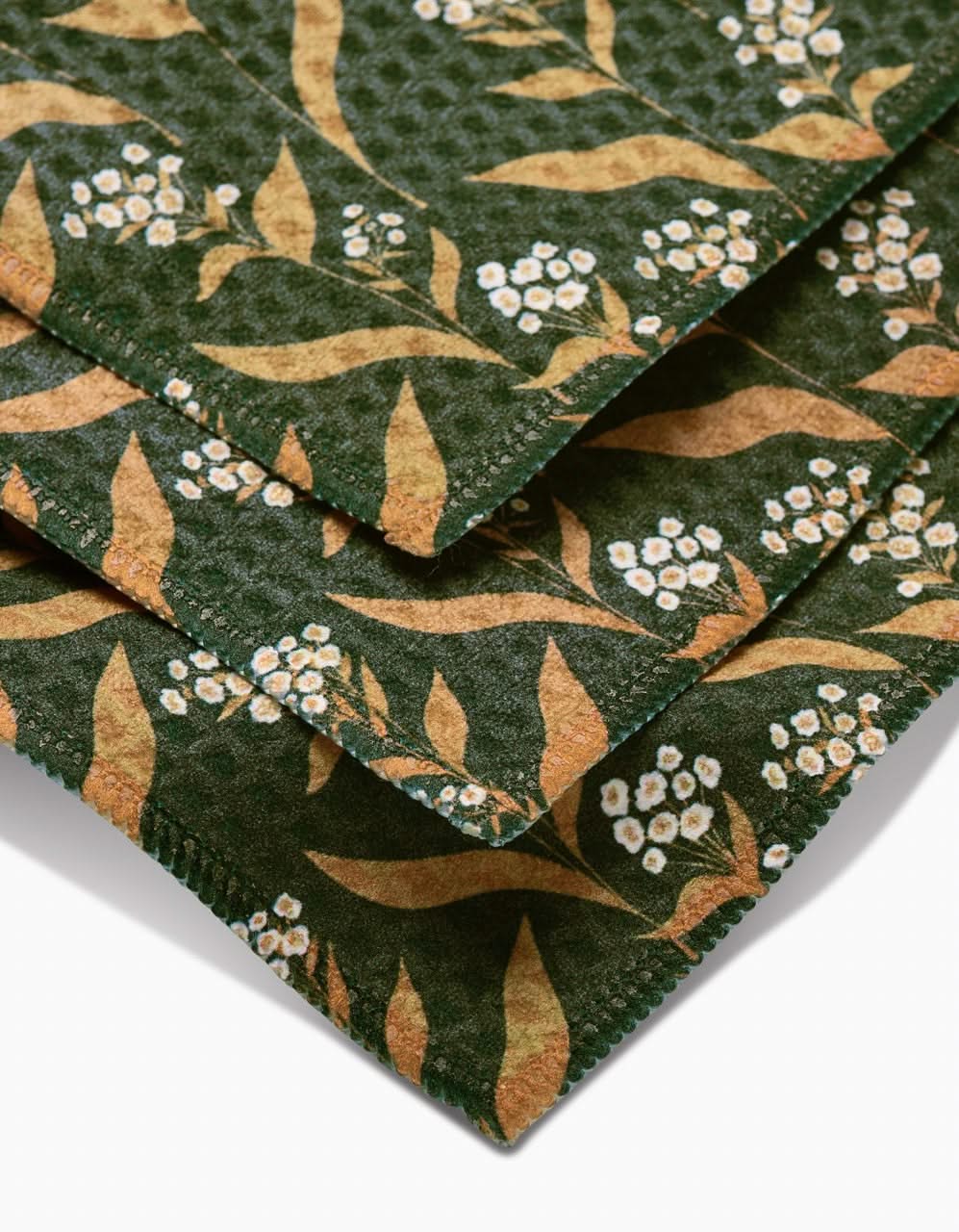 A close-up of Loretta washcloths by Charlie Rowan Designs shows folded green fabric with yellow leaves and white flowers, neatly stitched edges, and ultra-absorbent quality.
