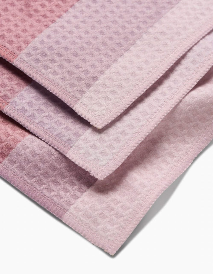 A close-up of three folded GEOMETRY Mauve Levels washcloths, showcasing a waffle texture and pink-purple gradient pattern, crafted with ultra-absorbent Geoweave technology.