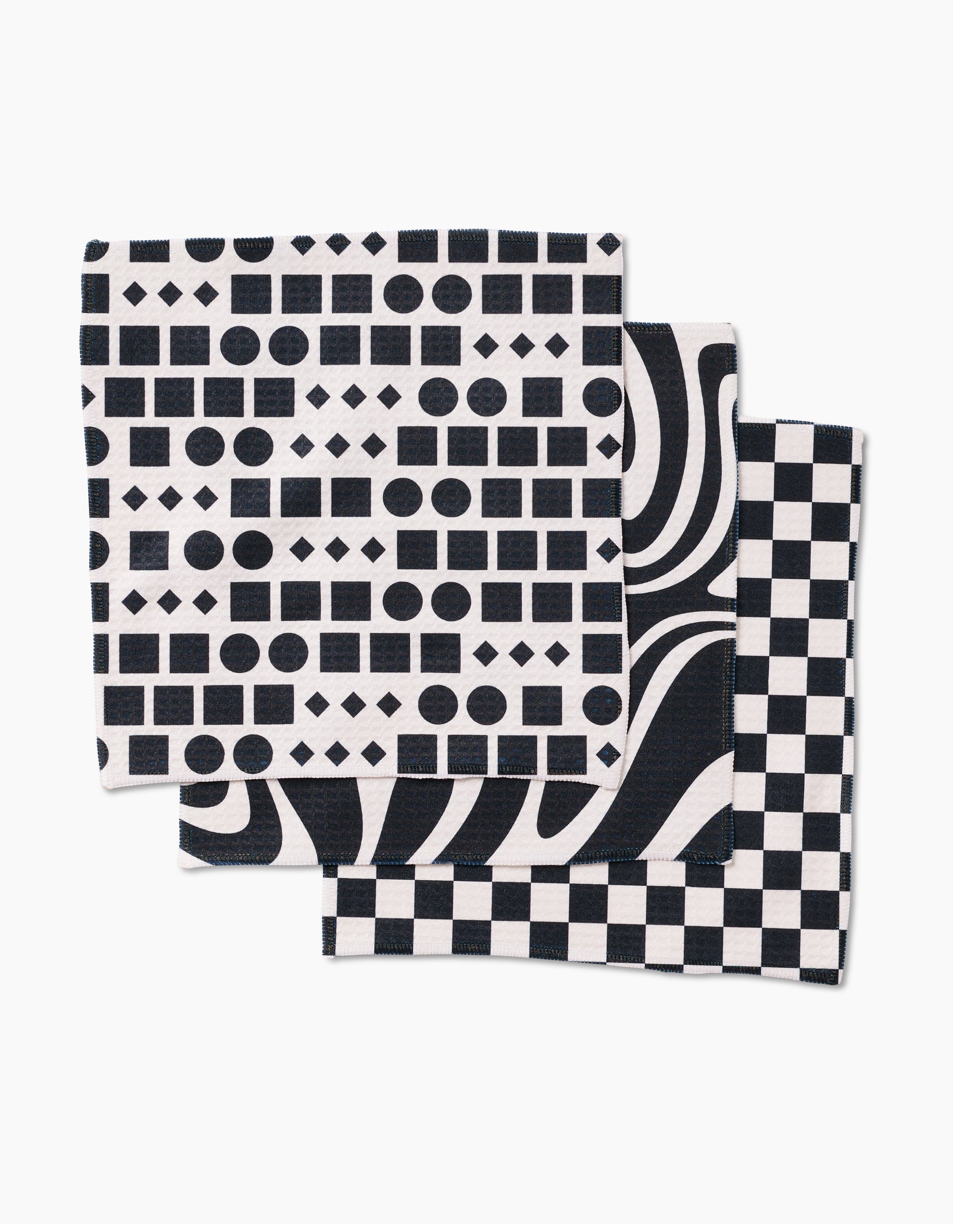 The GEOMETRY Mixed Up set includes three luxe washcloths with bold black and white geometric designs: one with dots, squares, and diamonds; one with wavy lines; and one in a classic checkerboard pattern.