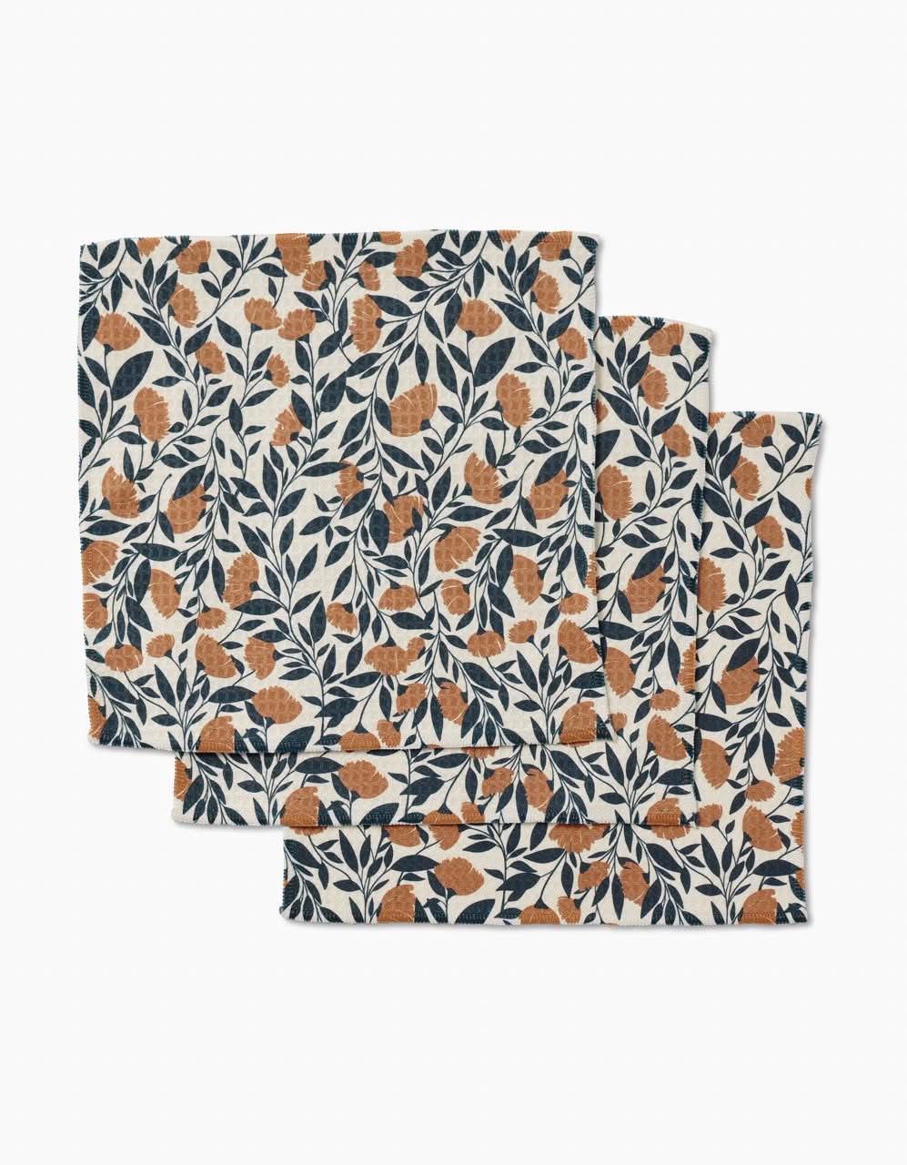 The Naomi napkins by Charlie Rowan Designs are a set of three, made from recycled materials, featuring an orange and navy leaf and fruit pattern on white, stacked with a slight offset.