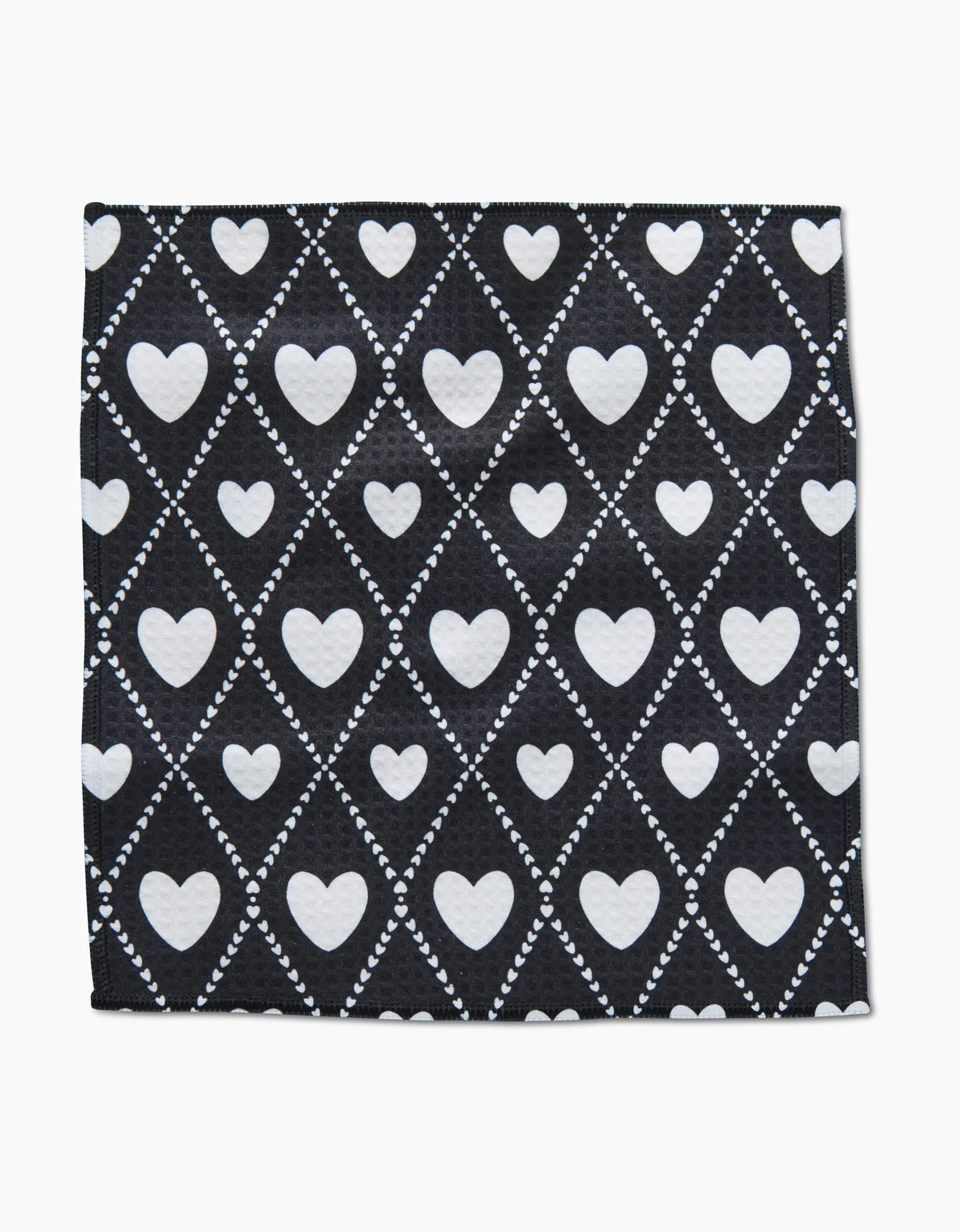 The Onyx Love Lattice washcloth by Charlie Rowan Designs is crafted from recycled materials and features a black base with white hearts in diamond shapes, outlined by dotted lines.