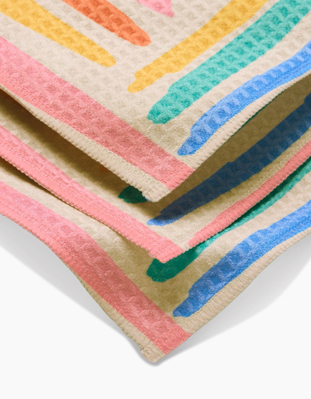 A close-up of Sareka Unique’s Pathways Luxe Washcloth in beige, with a waffle texture and colorful pink, orange, yellow, green, and blue striped edges—crafted using ultra-absorbent Geoweave technology for fast drying.