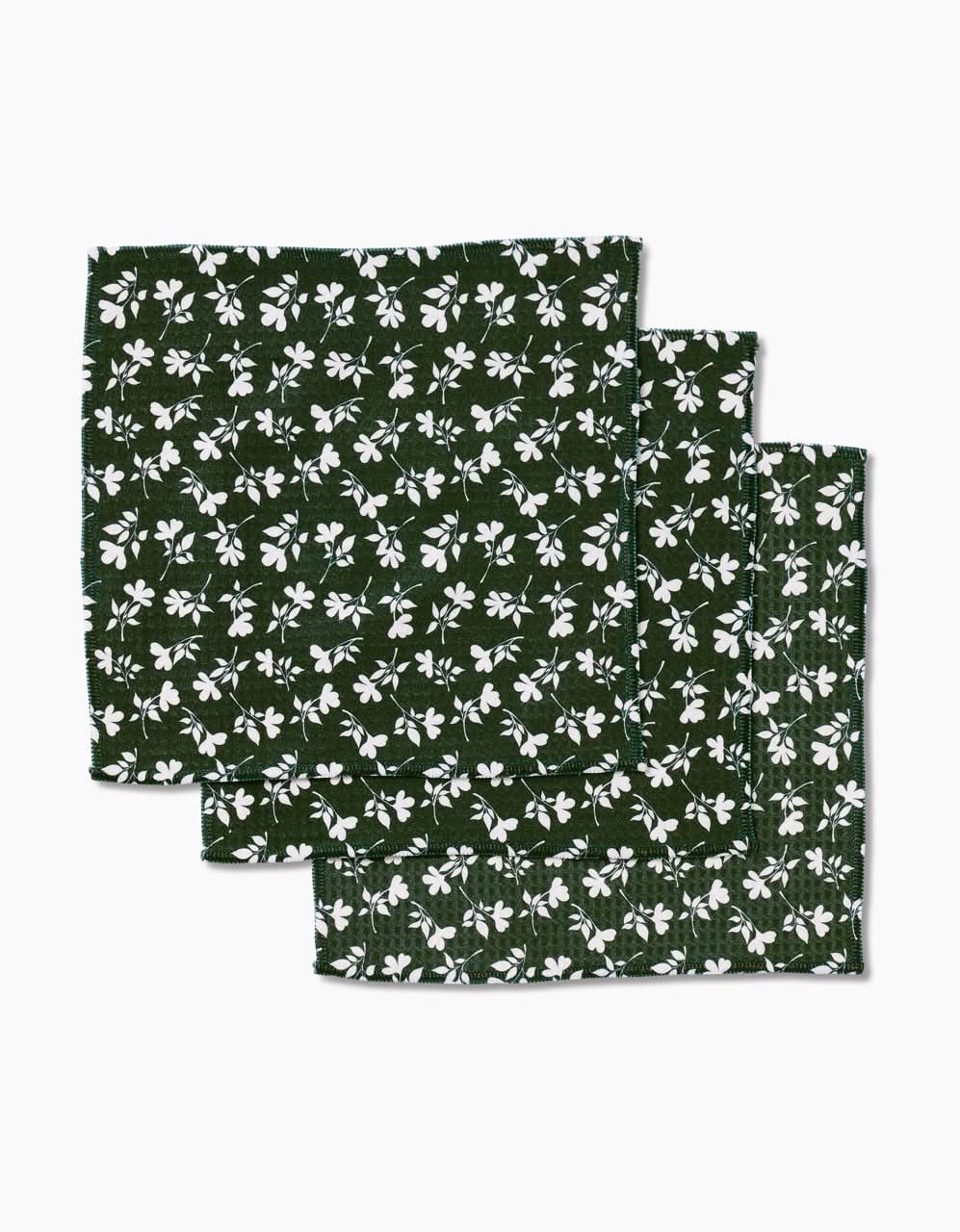 Three dark green Penelope Luxe Washcloth napkins by Charlie Rowan Designs, featuring a white floral pattern and crafted with Geoweave technology for ultra-absorbency, are neatly stacked against a white background.