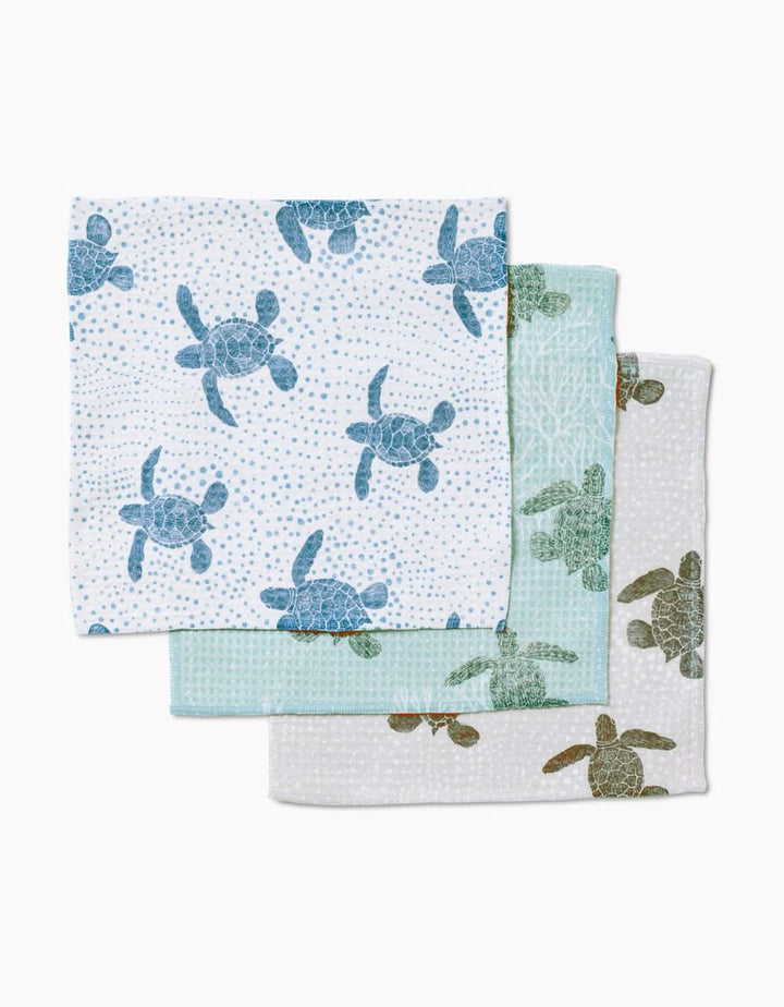 Three folded Katie O’Shea Sea Turtles Luxe Washcloths: blue turtles on white, teal turtles on green, and brown turtles on white—each crafted with ultra-absorbent Geoweave technology.