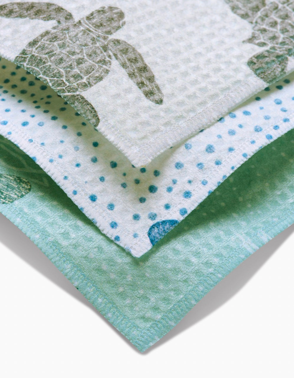 The Sea Turtles set by Katie OShea includes three stacked cloths: one with green sea turtles, one with blue polka dots and partial turtle design, and a solid light green—crafted with ultra-absorbent Geoweave technology.