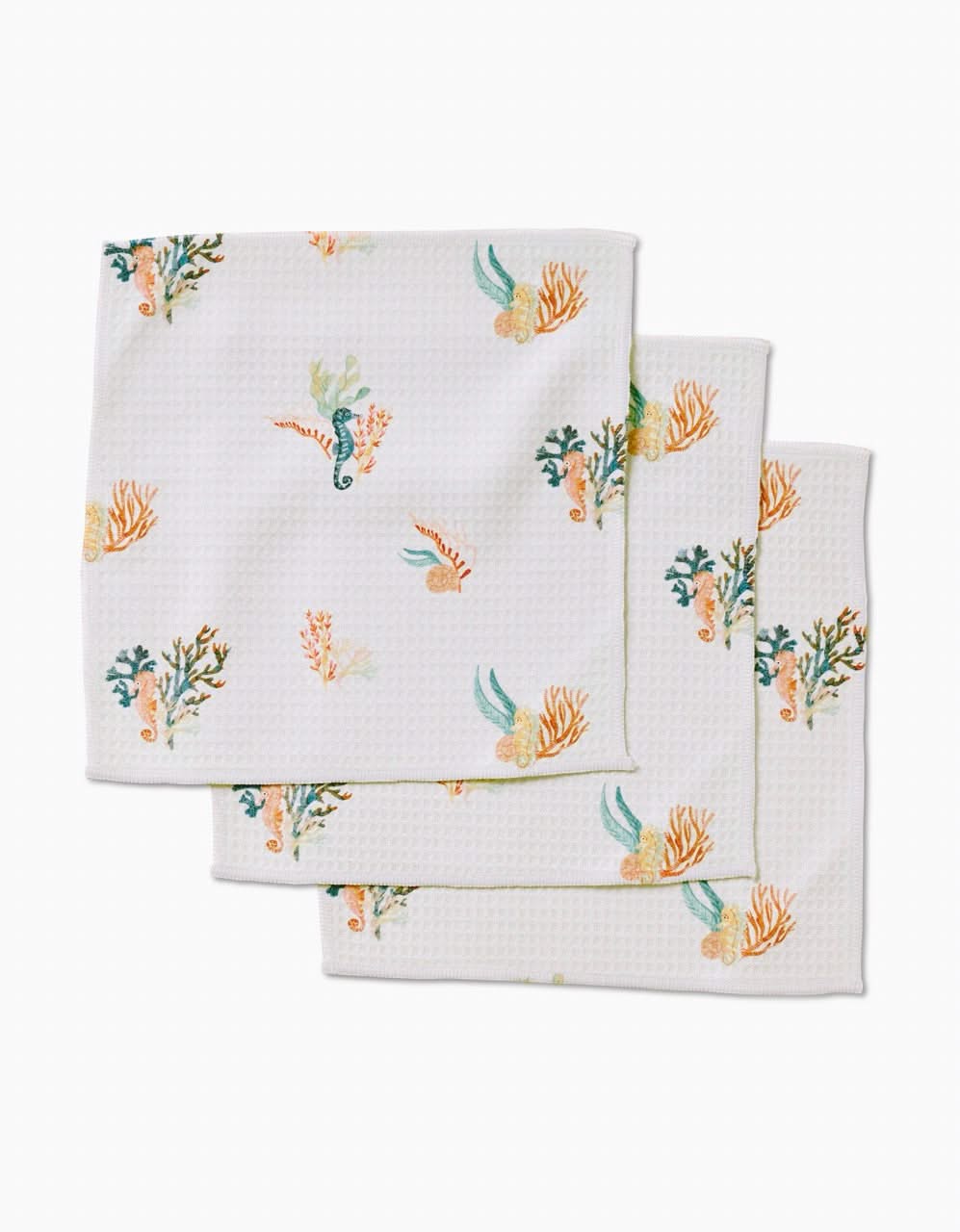 Three textured white cloth napkins from Janna Sue Design’s Seahorse Serendipity collection feature colorful sea-themed prints with seahorses, coral, and seaweed. Made from recycled washcloths for sustainable style.