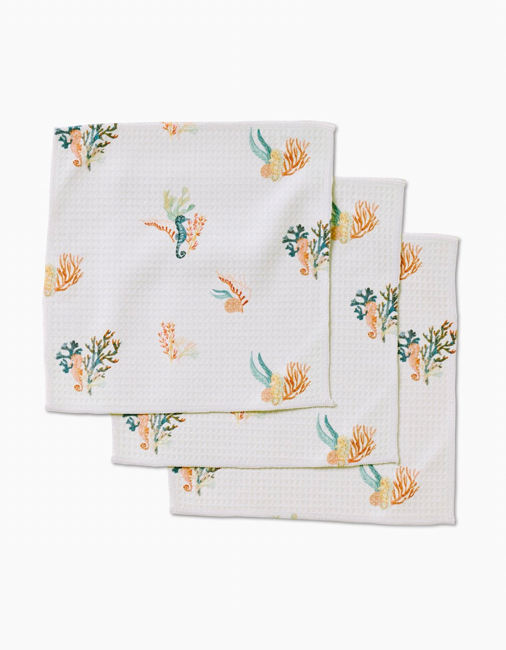 Three textured white cloth napkins from Janna Sue Design’s Seahorse Serendipity collection feature colorful sea-themed prints with seahorses, coral, and seaweed. Made from recycled washcloths for sustainable style.