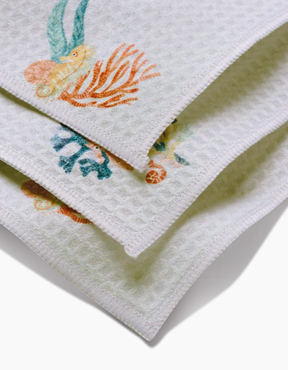 Close-up of three stacked Janna Sue Design Seahorse Serendipity washcloths, featuring a textured waffle pattern and colorful sea-themed coral, seaweed, and shell edges. These ultra-absorbent towels add style and function to any bathroom.