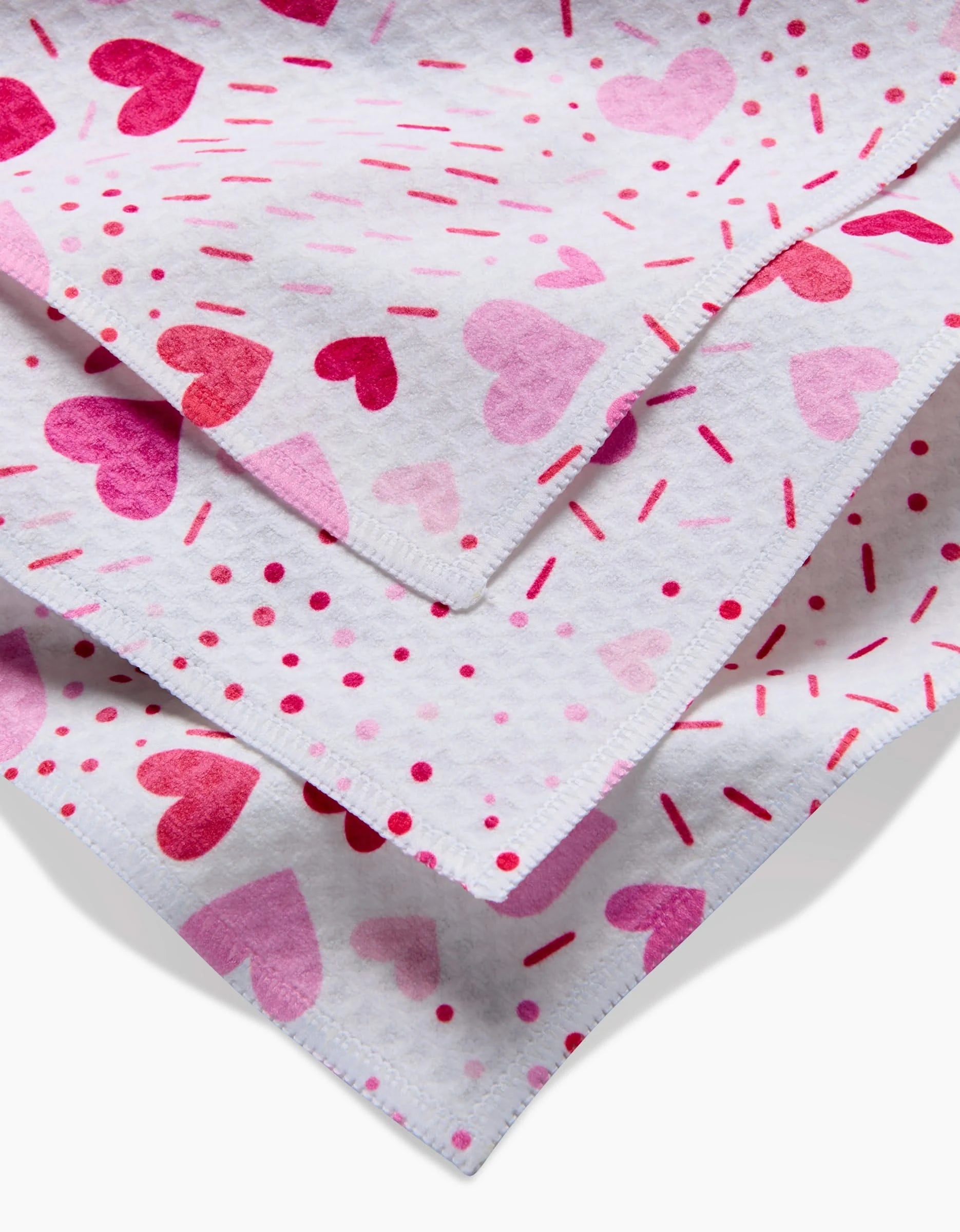 Close-up of three stacked Rebecca Bobko Sprinkled With Love washcloths, featuring pink and red heart patterns with matching dots and lines, set against a plain background.