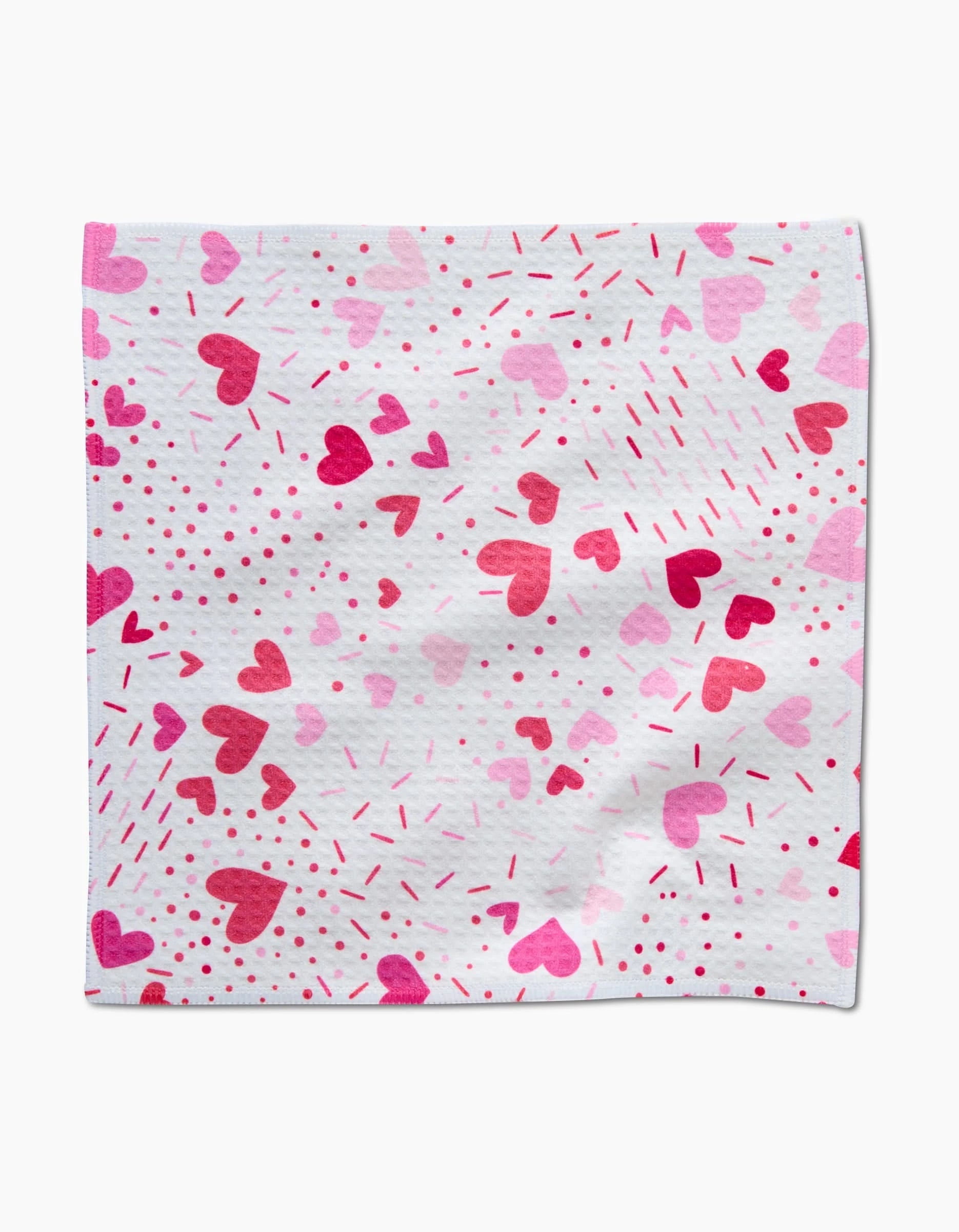 The Sprinkled With Love napkin by Rebecca Bobko features a white cloth adorned with pink and red hearts, dots, and lines—designed to perfectly complement our luxe washcloths.