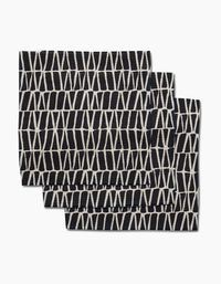 Three folded black Rosa Kichline Textured Geometry washcloths, each featuring a white geometric crisscross pattern, are shown overlapping on a plain white background.