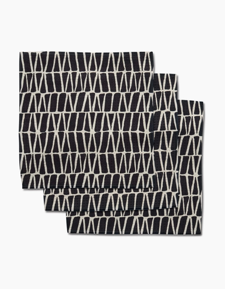 Three folded black Rosa Kichline Textured Geometry washcloths, each featuring a white geometric crisscross pattern, are shown overlapping on a plain white background.
