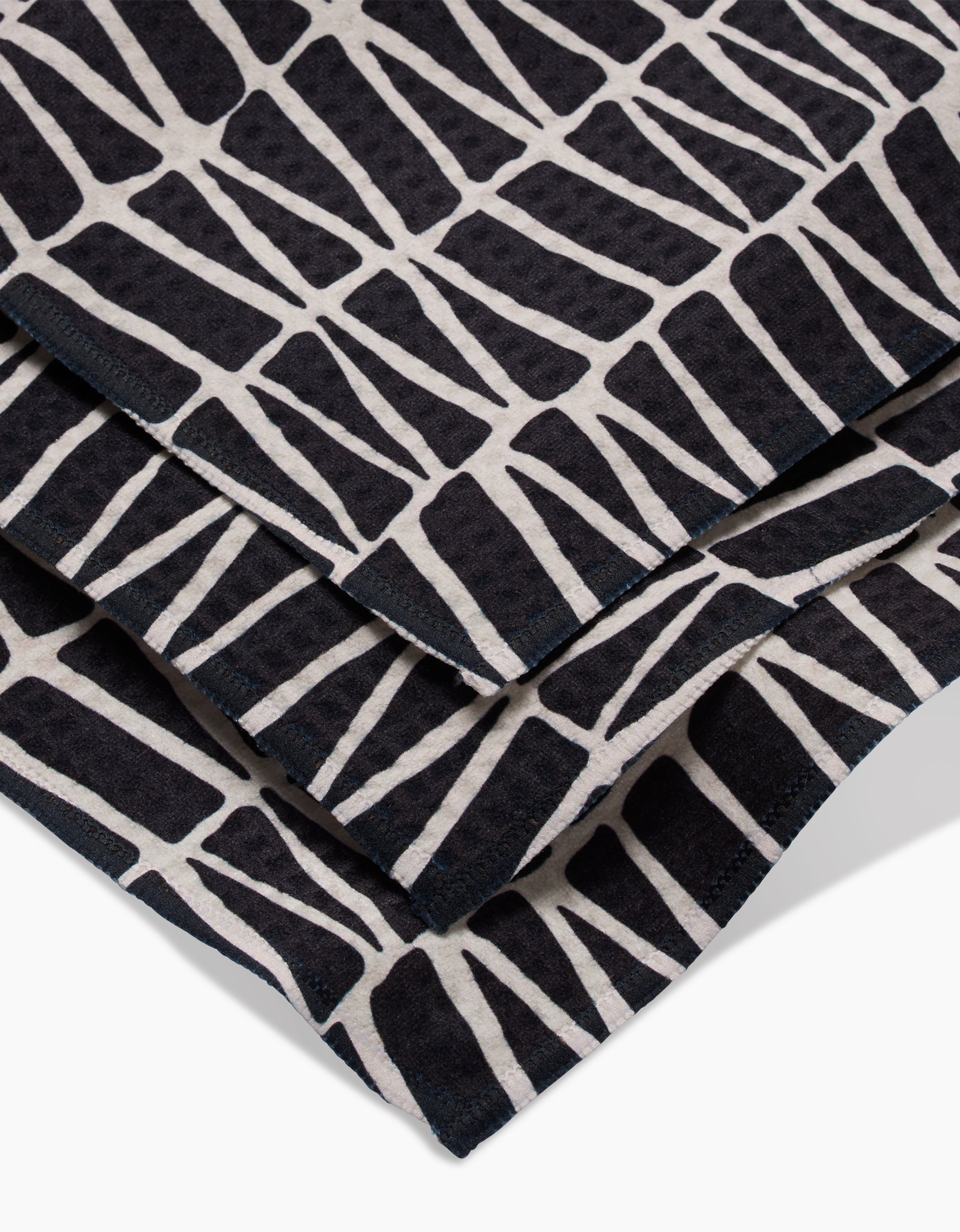 A close-up of Rosa Kichlines Textured Geometry towels—crafted from recycled materials—showcasing a bold black and white abstract pattern of irregular geometric blocks.
