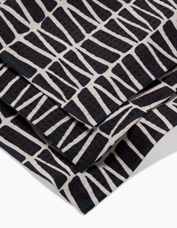 A close-up of Rosa Kichlines Textured Geometry towels—crafted from recycled materials—showcasing a bold black and white abstract pattern of irregular geometric blocks.