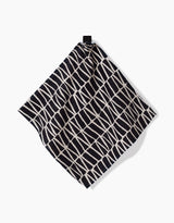 The Rosa Kichline Textured Geometry washcloth, featuring a black and white irregular grid pattern, hangs from a black loop against a plain white background.