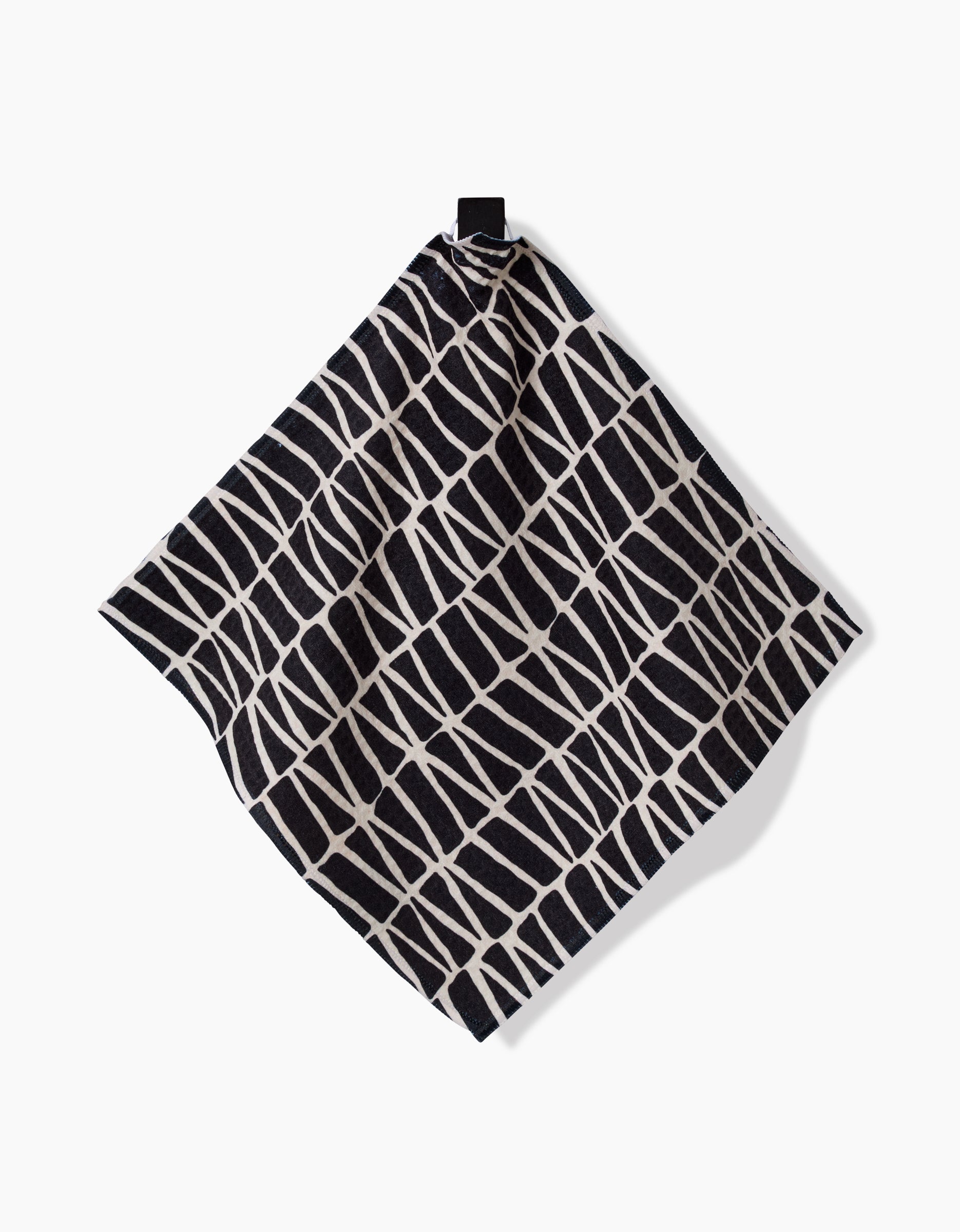 The Rosa Kichline Textured Geometry washcloth, featuring a black and white irregular grid pattern, hangs from a black loop against a plain white background.