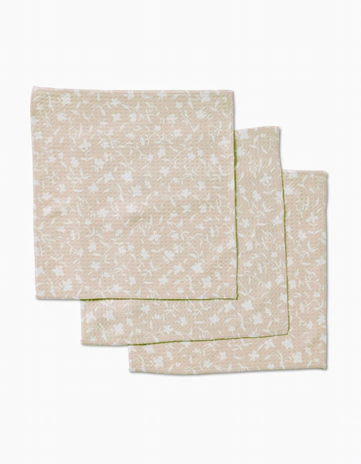 Three beige Tiny Floral cloth napkins by Aubrey Fairchild, featuring a subtle white floral pattern and crafted with ultra-absorbent Geoweave technology, are neatly stacked on a plain white background.